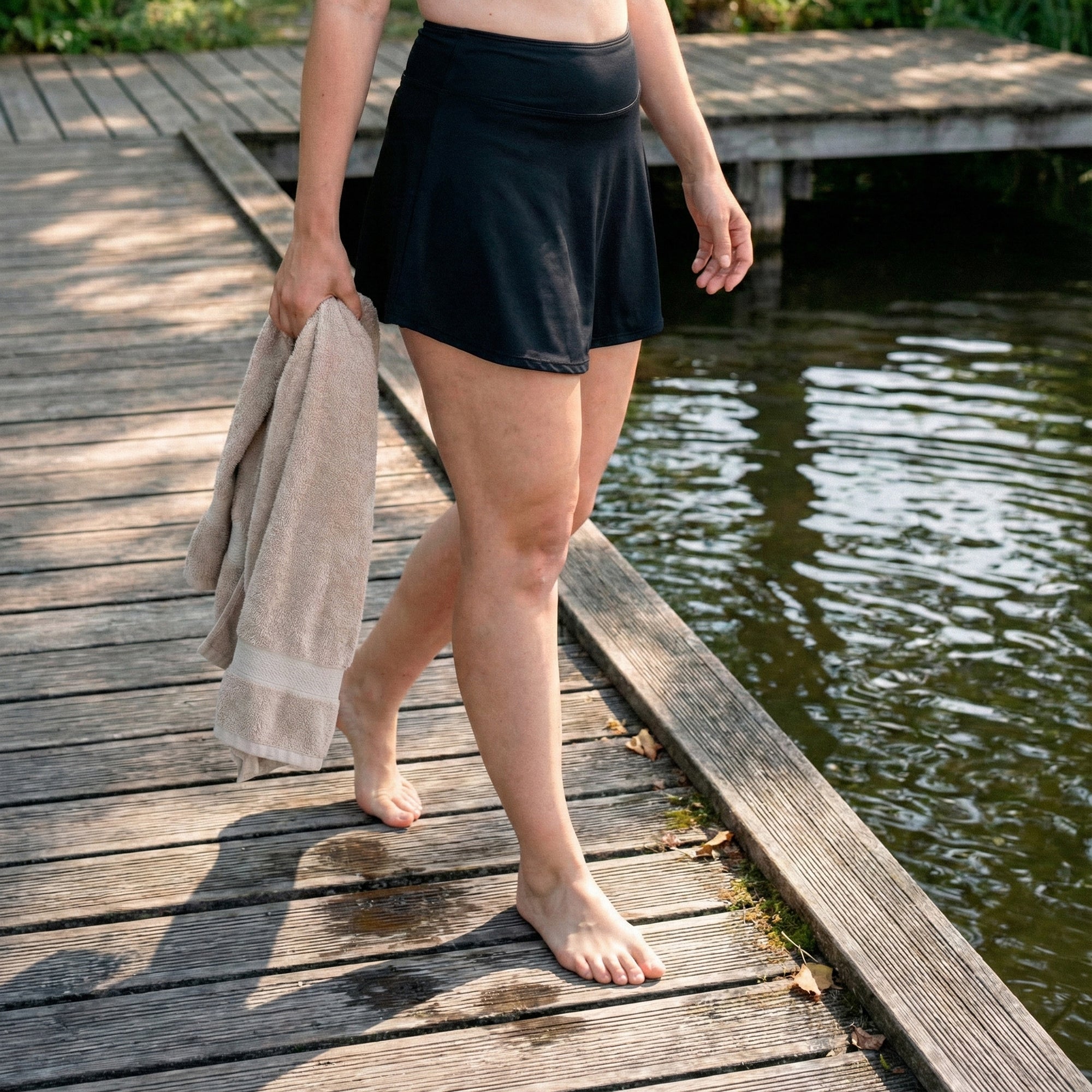 A woman walking beside the water in a black Floena period swim skirt