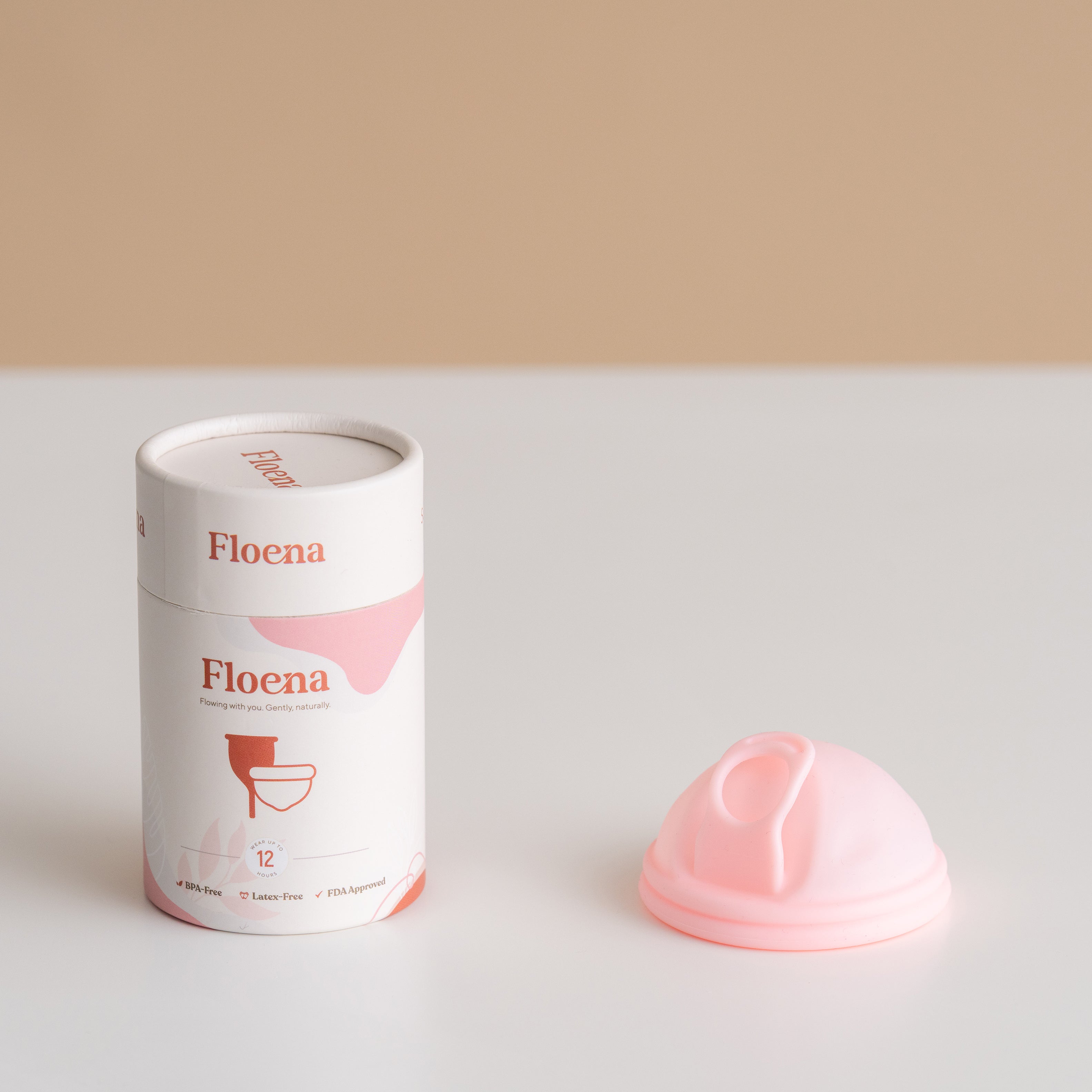 Floena Menstrual Disc — weiche rosa Menstruationsscheibe aus Silikon neben ihrer zylindrischen Verpackung in minimalistischem Setting