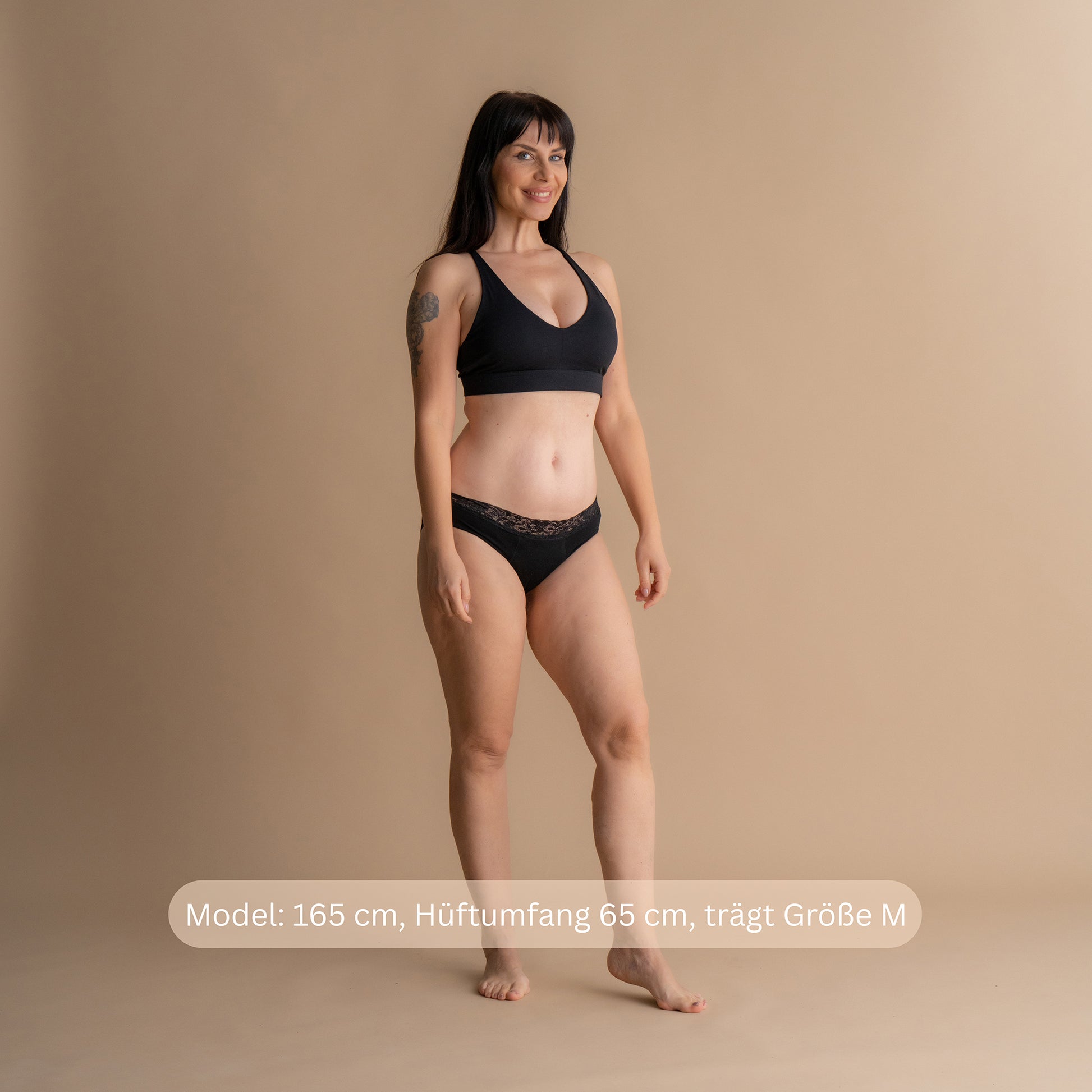 Model 165 cm groß, Hüftumfang 65 cm, trägt Größe M der Floena Leakproof Comfort Brief, schwarze Spitzen-Periodenunterwäsche, mit Größenhinweis