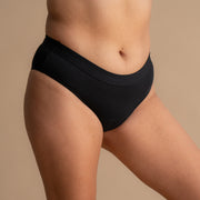 Vollständige Seitenansicht eines Models in der schwarzen Floena Leakproof Everyday Bamboo Bikini, Periodenunterwäsche aus Bambus, mit glattem Bund