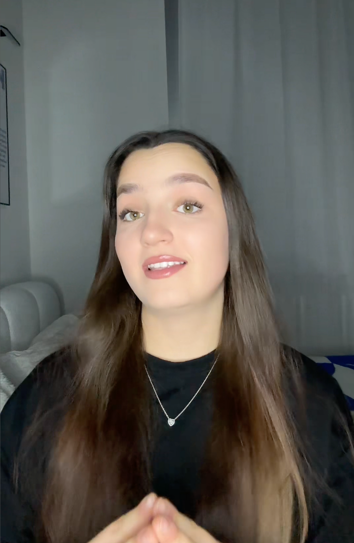 Woman with long brown hair wearing a black shirt and necklace in a room.
