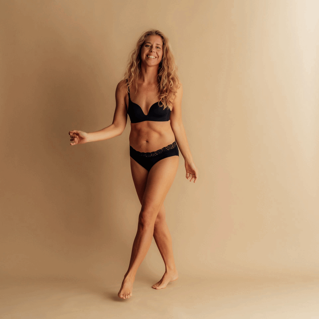 Frau trägt schwarze Leakproof Period Lace Brief, dehnt sich selbstbewusst mit einer entspannten Pose vor einem neutralen Hintergrund aus, was Komfort und Selbstvertrauen mit auslaufsicherem Schutz repräsentiert.
